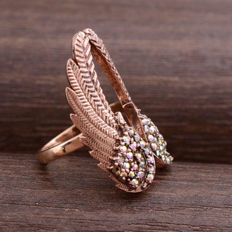 May include: A rose gold ring with a pair of wings adorned with iridescent rhinestones.