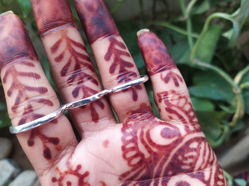 May include: A silver ring designed to be worn on multiple fingers. The ring is made of thick, textured metal and has a unique, asymmetrical shape.