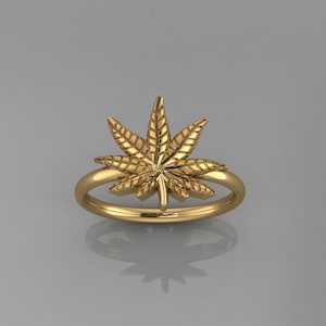 Könnte beinhalten: Ein goldener Ring mit einem detaillierten Marihuana-Blatt-Design.