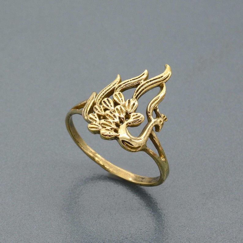 May include: A gold-toned ring featuring a detailed peacock design. The ring is made of metal and has a simple band.
