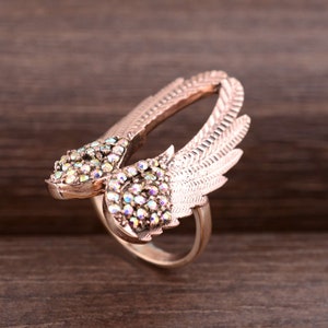 May include: A rose gold ring with a design of two wings set with iridescent rhinestones.