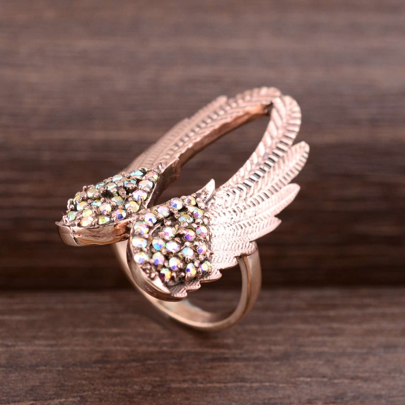 May include: A rose gold ring with a design of two wings set with iridescent rhinestones.