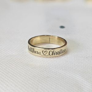 以下が含まれることがあります： ハートのシンボルで区切られた「Matthew」と「Christian」という名前が刻まれたゴールドのバンドリングです。