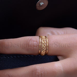 May include: Gold ring with a delicate, intricate design. The ring is made of three bands, each with a different pattern. The ring is worn on a finger.