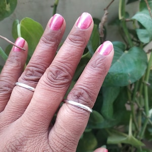 May include: A hand wearing two thin silver rings on the middle and ring fingers. The fingernails are painted a bright pink colour.