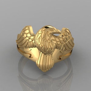 Può includere: Un anello d'oro con un designo di aquila. Le ali dell'aquila sono spiegate e la sua testa è girata di lato. L'anello è realizzato in metallo liscio e lucido.