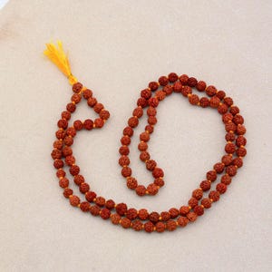 Puede incluir: Un collar de cuentas mala marrón con un borla amarilla. El collar está hecho de 108 cuentas y se utiliza para la meditación y la oración.