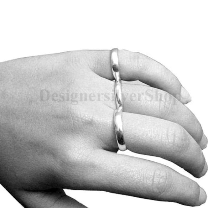 May include: A silver ring designed to be worn on multiple fingers. The ring is made of three connected bands that can be adjusted to fit different finger sizes.