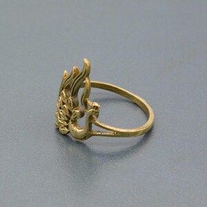 May include: A gold-toned ring with a peacock design. The peacock is facing to the right and has its wings spread out. The ring is made of metal and has a simple band.