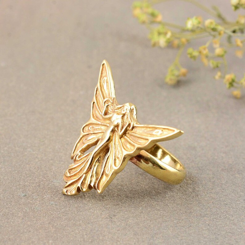 May include: A gold-toned ring featuring a detailed sculpted design of a fairy with wings spread wide.