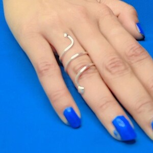 Puede incluir: Un anillo de plata con un diseño en espiral. El anillo se lleva en el dedo medio de una mano con esmalte de uñas azul.