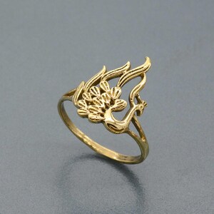 May include: A gold-toned ring featuring a detailed peacock design. The ring is made of metal and has a simple band.