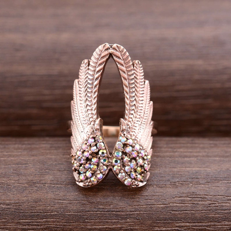 May include: A rose gold ring with a design of two wings with iridescent rhinestones. The wings are open and the ring is adjustable.