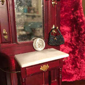 May include: A miniature wooden vanity with a marble top, a small mirror, and a beaded purse hanging on a hook. The vanity has a drawer with a gold handle.