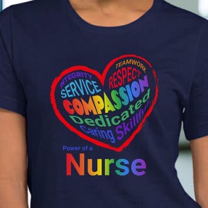May include: Navy blue t-shirt featuring a heart-shaped design with words like "Compassion" and "Service" in various colors. The text "Power of a Nurse" is below the heart.