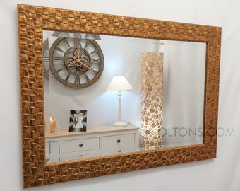May include: A large gold-toned mirror with a textured frame. The mirror is reflecting a room with a clock, a lamp, and a dresser.