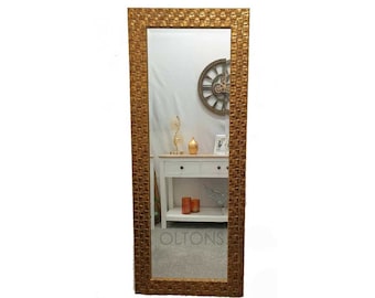 May include: A gold framed full-length mirror with a textured, mosaic-like design. The mirror is reflecting a room with a white dresser and a clock on the wall.