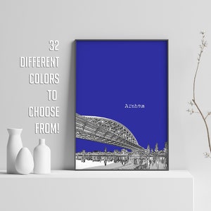 Op de afbeelding: Een zwart-witte illustratie van een brug over een skyline van een stad. De achtergrond is effen blauw. De tekst "Arnhem" is in wit bovenaan de afbeelding gedrukt.