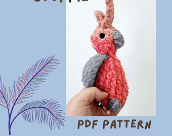 Op de afbeelding: Een gehaakt knuffeldier in de vorm van een Galah, een roze en grijze Australische papegaai. Het speelgoed wordt vastgehouden door een hand. De tekst "MINI GALAH STUFFIE PDF PATTERN" staat onderaan de afbeelding.