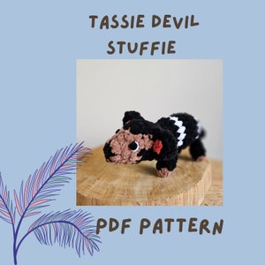 Puede incluir: Patrón de crochet para un animal de peluche en forma de diablo de Tasmania. El patrón está disponible para descargar en PDF. La imagen muestra un diablo de Tasmania de crochet con pelaje negro y blanco, ojos marrones y una nariz rosa.