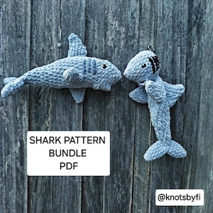 May include: Two crocheted shark plushies in shades of gray and blue. The plushies are displayed against a wooden background. The text "SHARK PATTERN BUNDLE PDF" and "@knotsbyfi" are visible in the image.