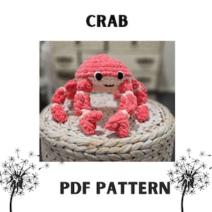 Pode incluir: Um brinquedo de crochê de caranguejo rosa e branco com olhos pretos e uma boca sorridente. O caranguejo está sentado em uma cesta tecida. O texto "CRAB" está acima da imagem e "PDF PATTERN" está abaixo da imagem.