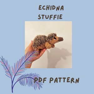 May include: A crocheted echidna stuffed animal in brown and gray. The stuffed animal is being held in a hand. The image includes the text "Echidna Stuffie PDF Pattern".