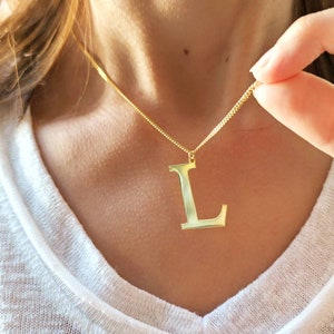Può includere: Una collana con catena d'oro con un ciondolo a forma di lettera L dorata.