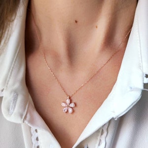 Puede incluir: Un delicado collar de oro rosa con un colgante de flor rosa. La flor está hecha de pequeñas piedras en forma de pera.