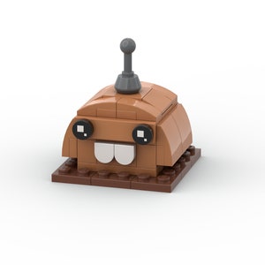 Puede incluir: Un modelo de Lego de color marrón y gris de una criatura con una cara sonriente, dos ojos negros y una sola antena en la parte superior de su cabeza.