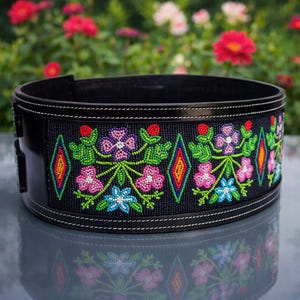 Puede incluir: Cinturón de cuero negro con intrincado trabajo de cuentas. El cinturón presenta un diseño floral con cuentas rosas, moradas, azules y verdes. El diseño incluye formas de diamante en rojo, naranja y amarillo. Costuras blancas acentúan los bordes.