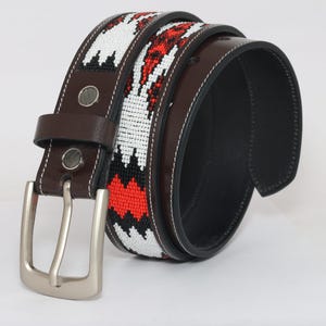 May include: A brown leather belt with a white, red, and black woven design. The belt has a silver buckle.