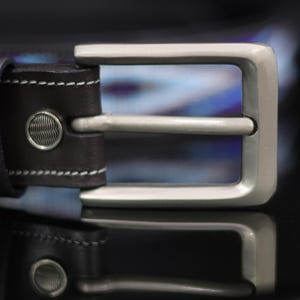 Op de afbeelding: Een donkerbruine leren riem met een rechthoekige gesp van geborsteld zilverkleurig metaal en een bijpassende leren lus. De riem is afgewerkt met witte contraststiksels en twee ronde zilveren klinknagels met een textuurpatroon.