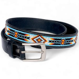 May include: A black leather belt with a beaded design. The belt has a silver-coloured buckle and white stitching. The beaded pattern includes blue, orange, white, and black geometric shapes.