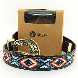 May include: A black leather belt with a colourful beaded design and a gold-tone buckle. The belt is packaged in a brown box with the brand name "MEYAR BE THE BEST..." printed on it.