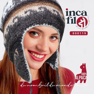 May include: A grey and white knitted hat with ear flaps. The hat has a geometric pattern and is made of 100% alpaca wool. The hat is being worn by a person with a red shirt. The text "inca fil" and "du nombril du monde" is visible in the image.