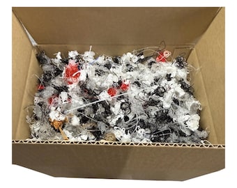 May include: A cardboard box filled with a tangled assortment of colorful plastic pieces. The pieces are primarily black, white, and red, with some clear and orange elements. The box is open, revealing the contents.