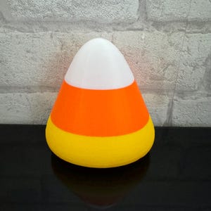 Può includere: Un'illuminazione notturna a forma di caramella di mais bianca, arancione e gialla.