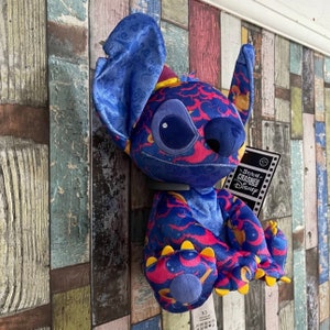 May include: Blue and pink Stitch plush toy with a cloud pattern. The toy is wearing a blue hat and has a Stitch Crashes Disney tag.