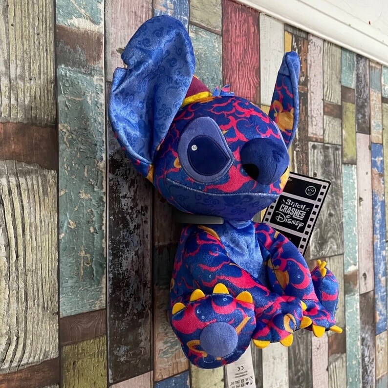 May include: Blue and pink Stitch plush toy with a cloud pattern. The toy is wearing a blue hat and has a Stitch Crashes Disney tag.