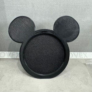 May include: Black plastic Mickey Mouse-shaped phone stand with a circular base and two large ears.
