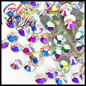 May include: Assortment of iridescent clear glass rhinestones in various sizes. The rhinestones have a rainbow effect and are scattered on a white surface.