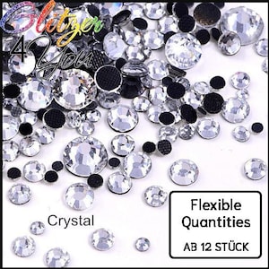 Op de afbeelding: Een verzameling heldere, gefacetteerde ronde strass-steentjes van verschillende groottes gemengd met kleine zwarte ronde platte versieringen. De afbeelding bevat de tekst Glitzer 4 You, Crystal en een kader met Flexible Quantities AB 12 STÜCK.