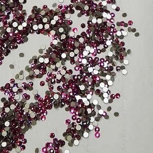 Peut inclure: Une dispersion de petits strass ronds et irisés roses sur une surface blanche.