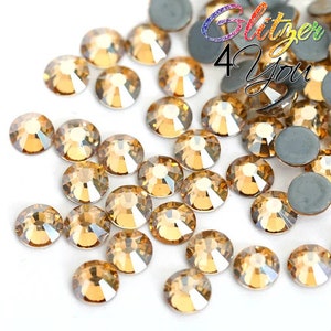 Op de afbeelding: Een close-up afbeelding van een verstrooiing van kleine, ronde, heldere glazen strasssteentjes met een gouden amberkleur. De strasssteentjes zijn verspreid over een wit oppervlak. De afbeelding bevat de tekst "Glitter 4 You".