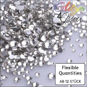 Op de afbeelding: Een verzameling heldere, gefacetteerde, ronde strass-steentjes van verschillende groottes verspreid over een oppervlak. De afbeelding bevat de tekst Glitzer 4 You, Flexible Quantities en AB 12 STÜCK in de rechterboven- en rechterbenedenhoek.