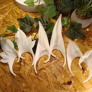 Könnte beinhalten: Sechs weiße Elfenohren aus glattem, hartem Kunststoff. Die Ohren sind in verschiedenen Formen und Größen, einige haben eine spitze Spitze und andere eine abgerundete Spitze.