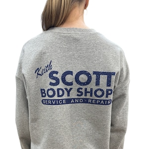 May include: A gray sweatshirt with a navy blue print on the back that says "Keith Scott Body Shop Service and Repair."