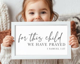 Puede incluir: Un cartel enmarcado en blanco con el texto "for this child we have prayed 1 Samuel 1:27" en letras grises. Un niño pequeño sostiene el cartel frente a él.
