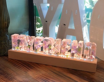 May include: A wooden sign with the word "Boyfriend" spelled out in clear resin letters. Each letter is filled with dried pink and purple flowers.